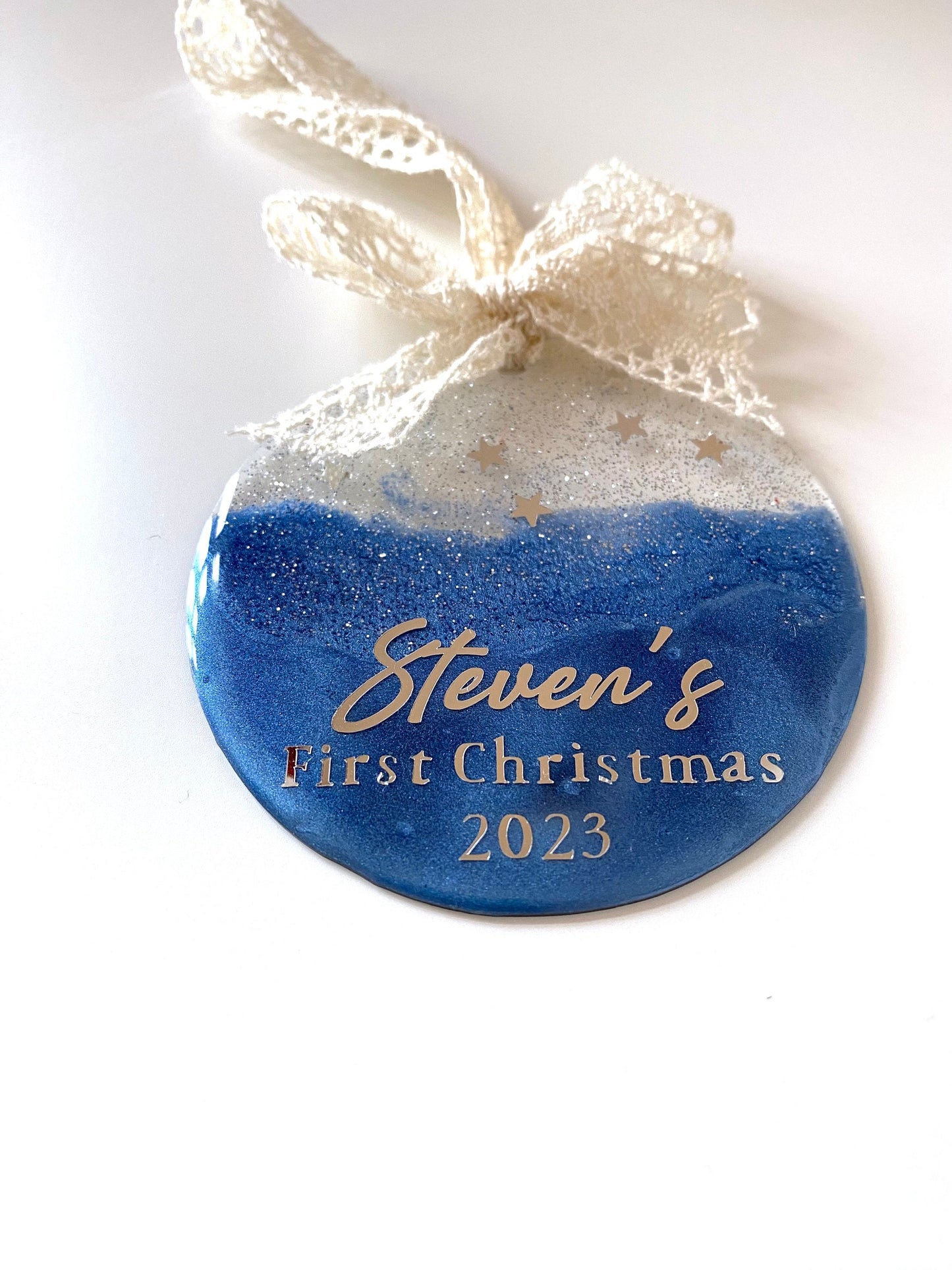 Blue Baby First Christmas resin bauble with glittery silver top and twinkling stars, personalised with "1st Christmas" in silver lettering, hanging with beige lace ribbon and bow