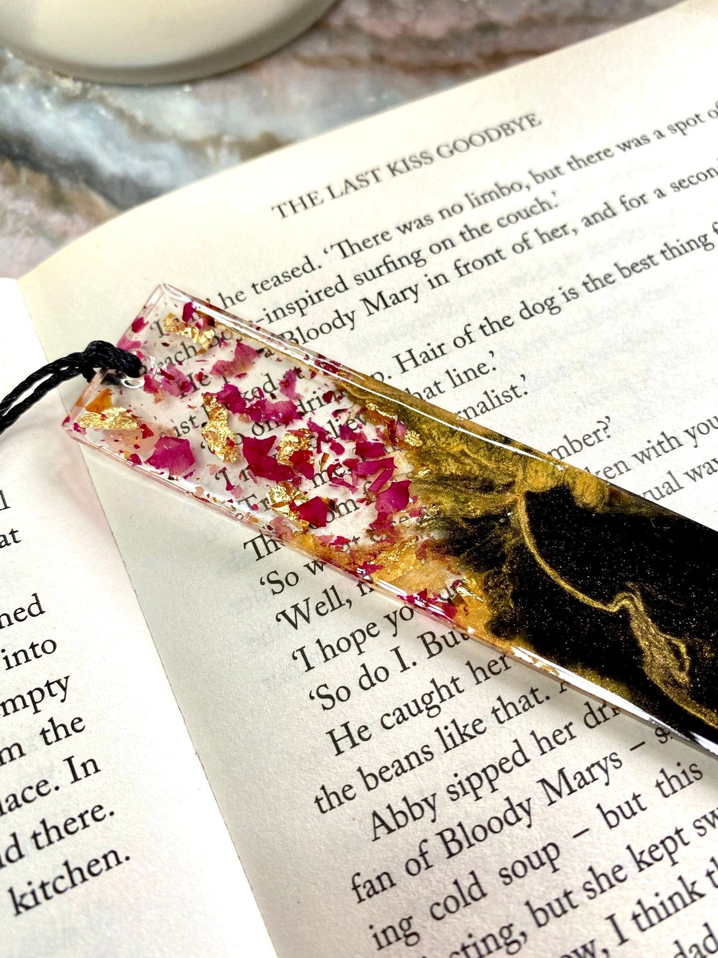 Close-up of black and gold resin bookmark showing dried rose petals in clear resin with gold leaf accents