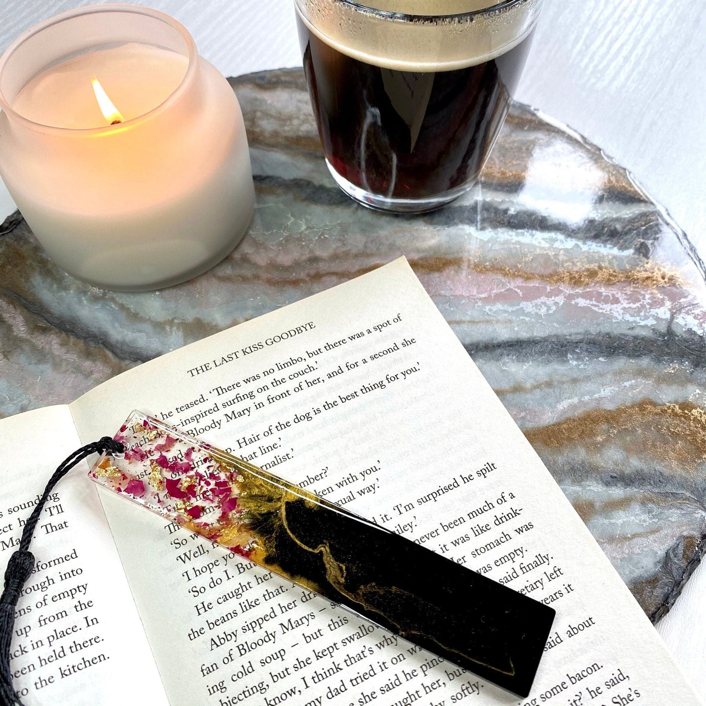 Floral black resin bookmark on an open book with a lit candle and coffee cup in the background