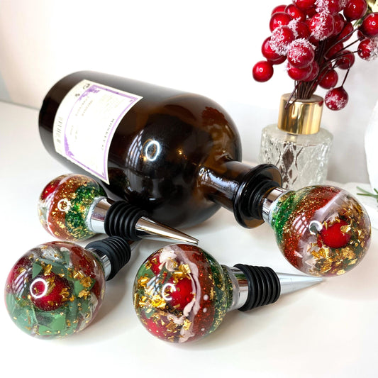 Christmas resin wine stopper in wine bottle with additional stoppers on surface, showing red berries, gold leaf, and glitter details