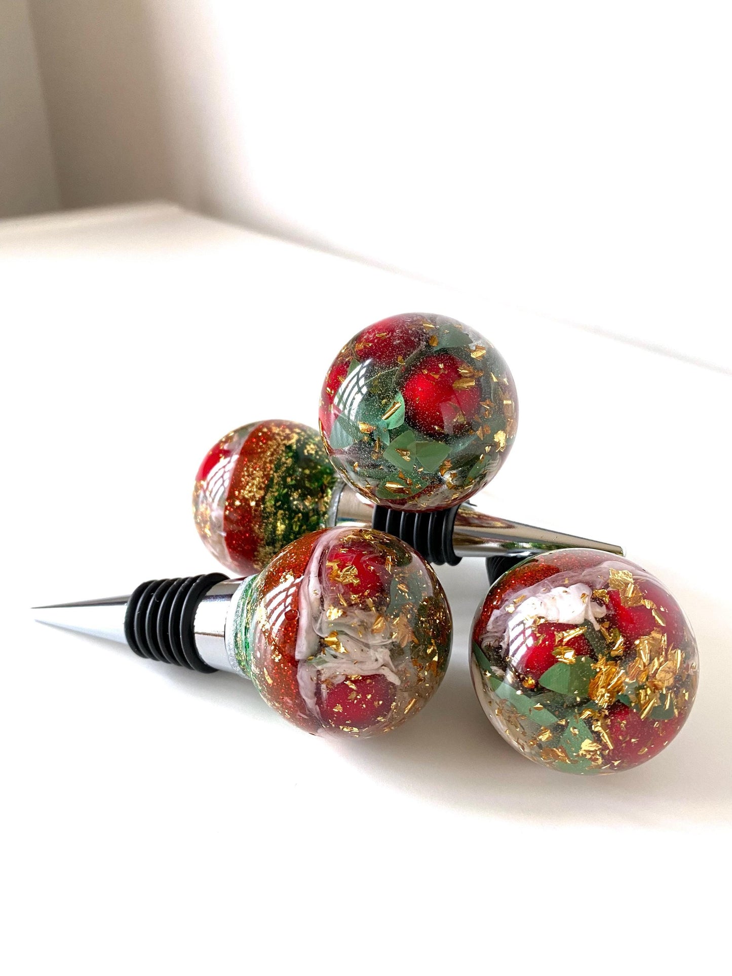 Four Christmas resin wine stoppers stacked showing detailed resin design with red berries, gold leaf, and glitter accents