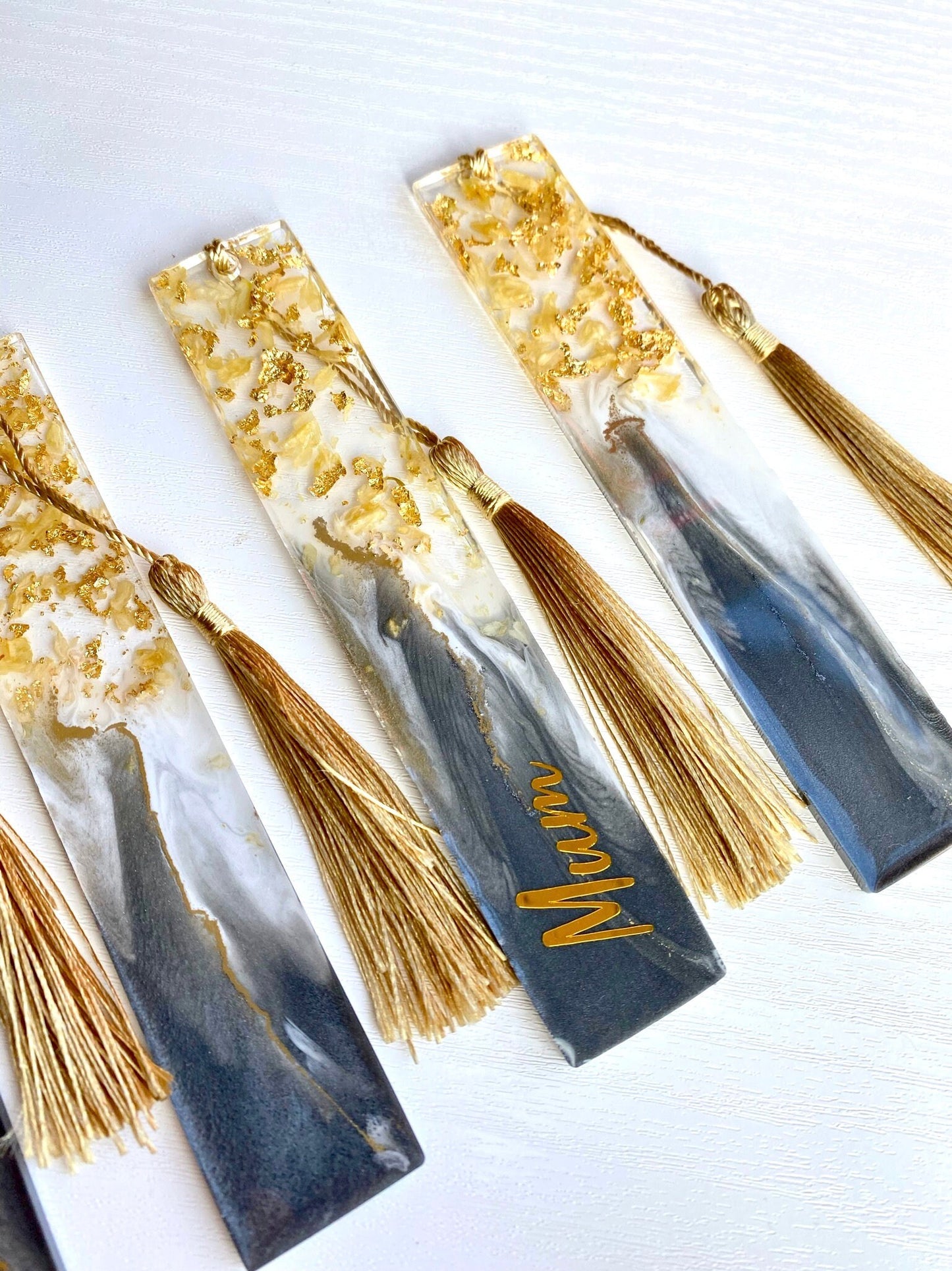 Close-up of five grey resin bookmarks with dried jasmine petals and gold leaf, showing handmade details and gold tassels, personalised and non-personalised options, ideal gift bookmarks for readers.