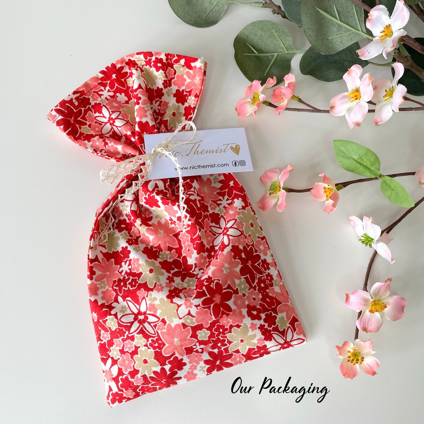 Fabric gift bag for handmade lace hair bow clips, used for packaging bows before shipping, displayed on white surface with flowers in the background