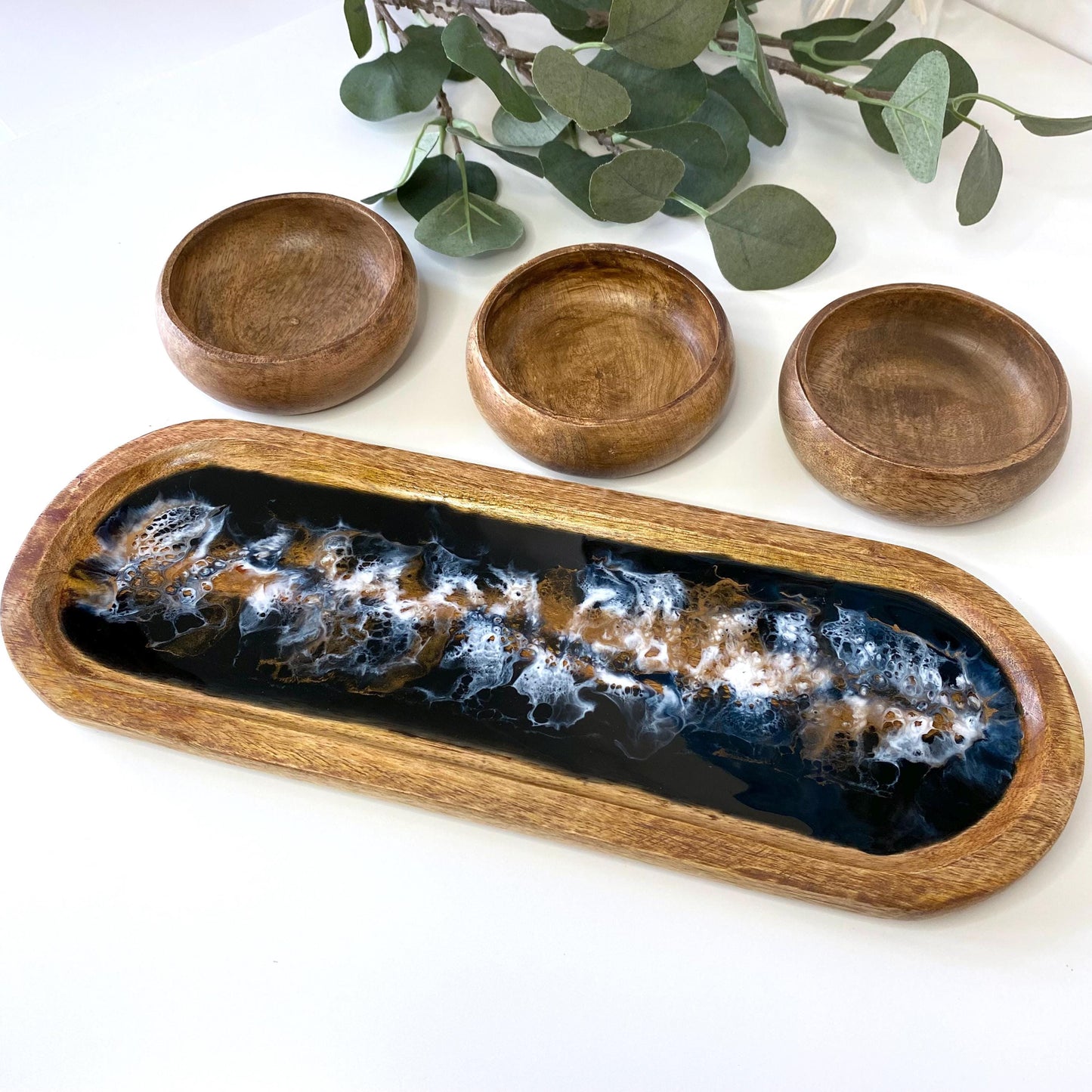 Large handcrafted wooden oval tray with swirling epoxy resin details, shown from an angled view with three plain wooden bowls – versatile for charcuterie, serving, or home décor.