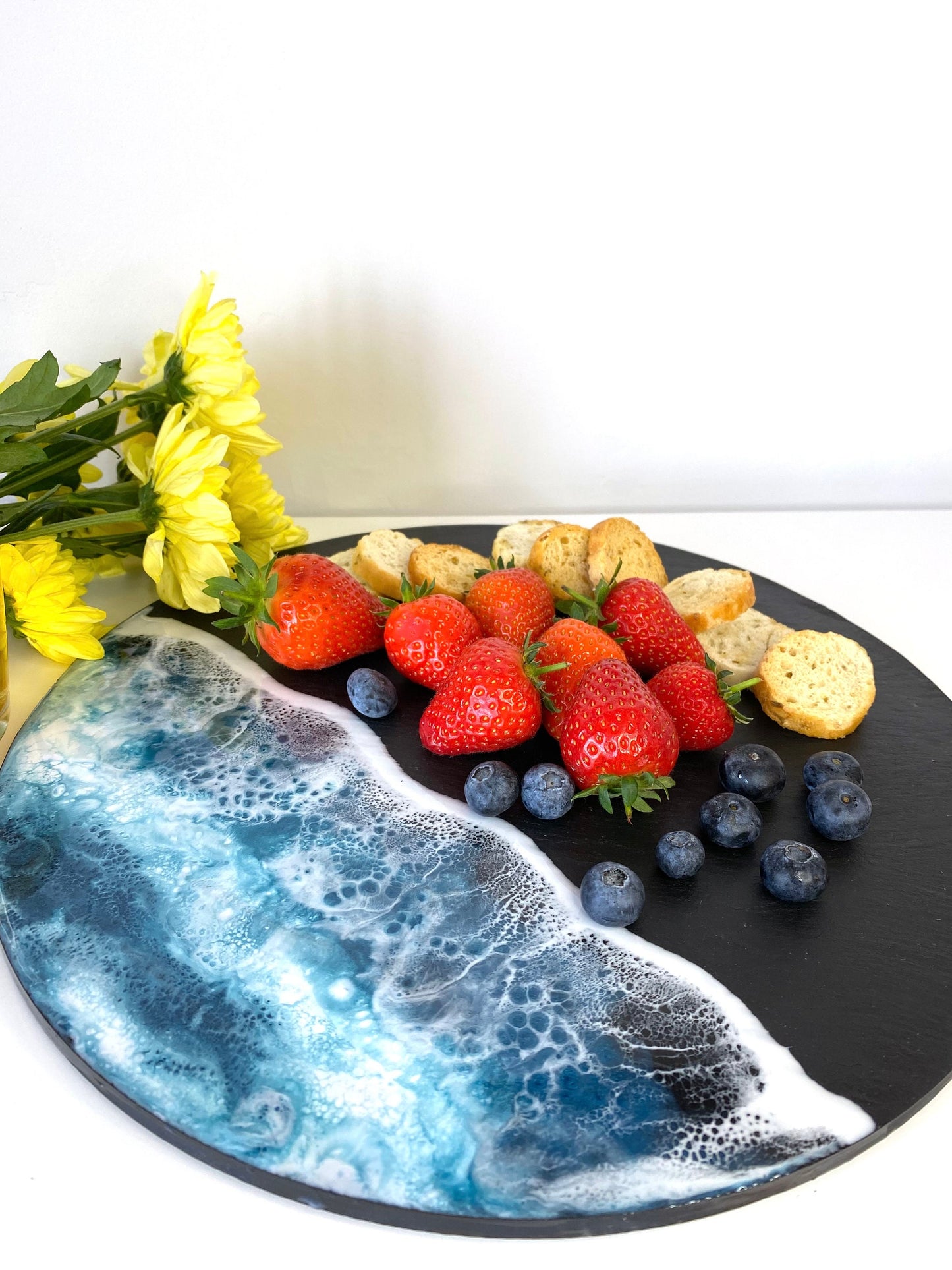Close-up of handmade ocean resin charcuterie tray with slate base, showing crackers, strawberries and blueberries, highlighting coastal-inspired design and craftsmanship for serving or display.