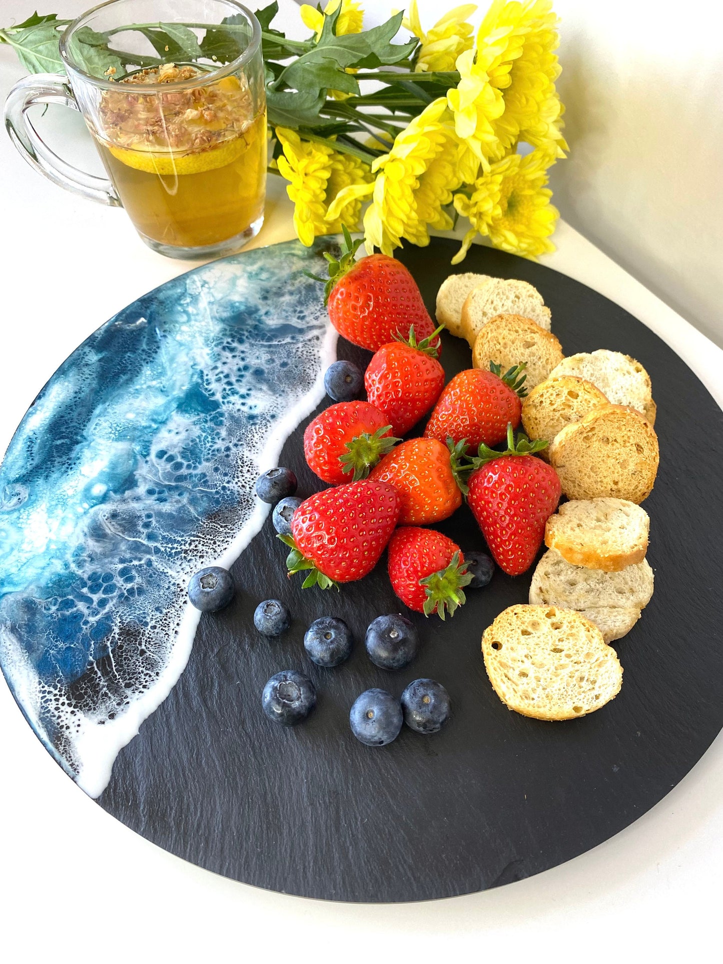 Top-down view of handmade ocean resin charcuterie tray with slate base, styled with crackers, strawberries and blueberries, coastal-inspired serving and cheese board for entertaining