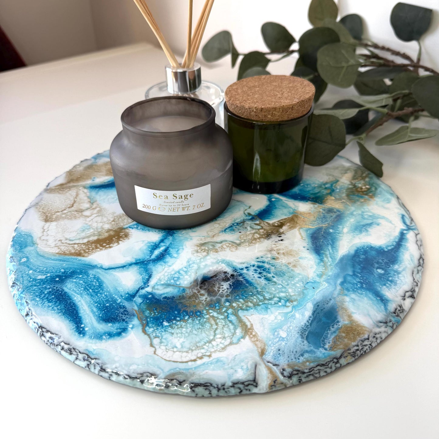 Handmade ocean resin tray with slate base on table, styled with candles and diffuser, leaves in the background, showcasing coastal-inspired decorative home use