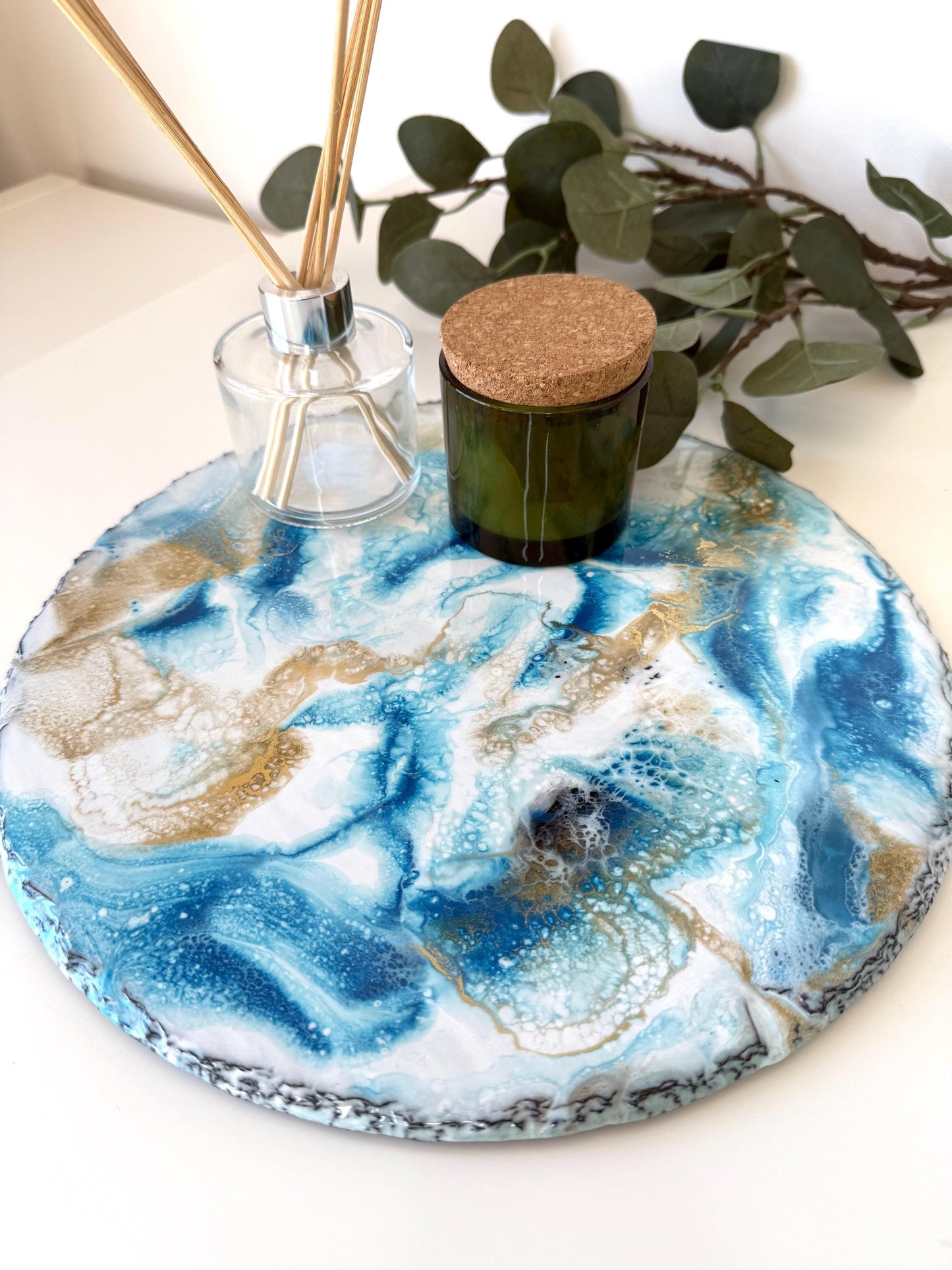 Top-down close-up of handmade ocean resin tray with slate base, styled with candles and diffuser, showcasing blue and white resin waves, coastal-inspired decorative tray for home display
