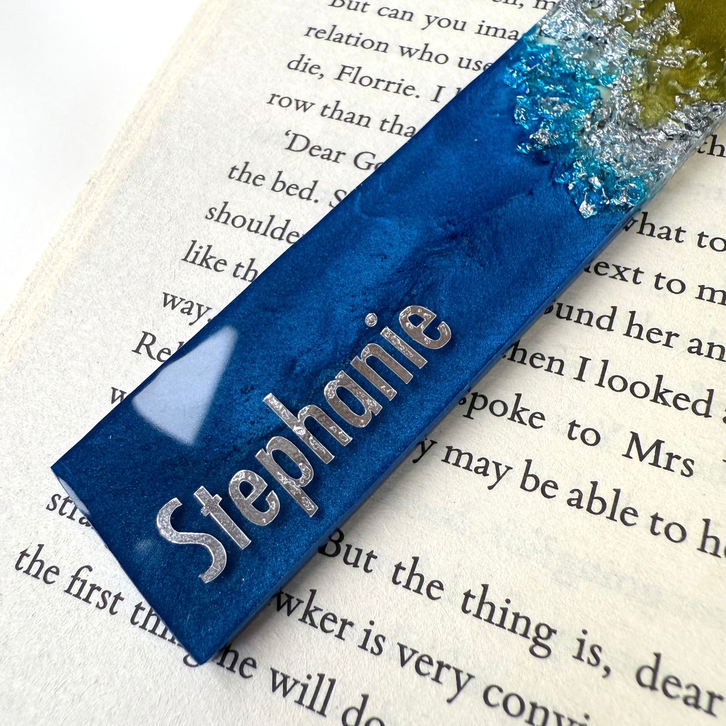Close-up of personalised resin bookmark showing silver vinyl name. Handmade blue, green, and silver celestial-inspired bookmark, ideal gift for book lovers
