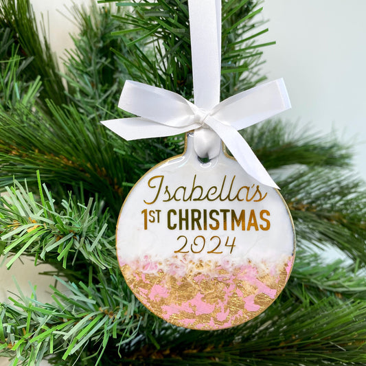 Personalised pink slate resin baby’s first Christmas bauble hanging on a Christmas tree, customised with baby’s name and First Christmas 2025 in gold