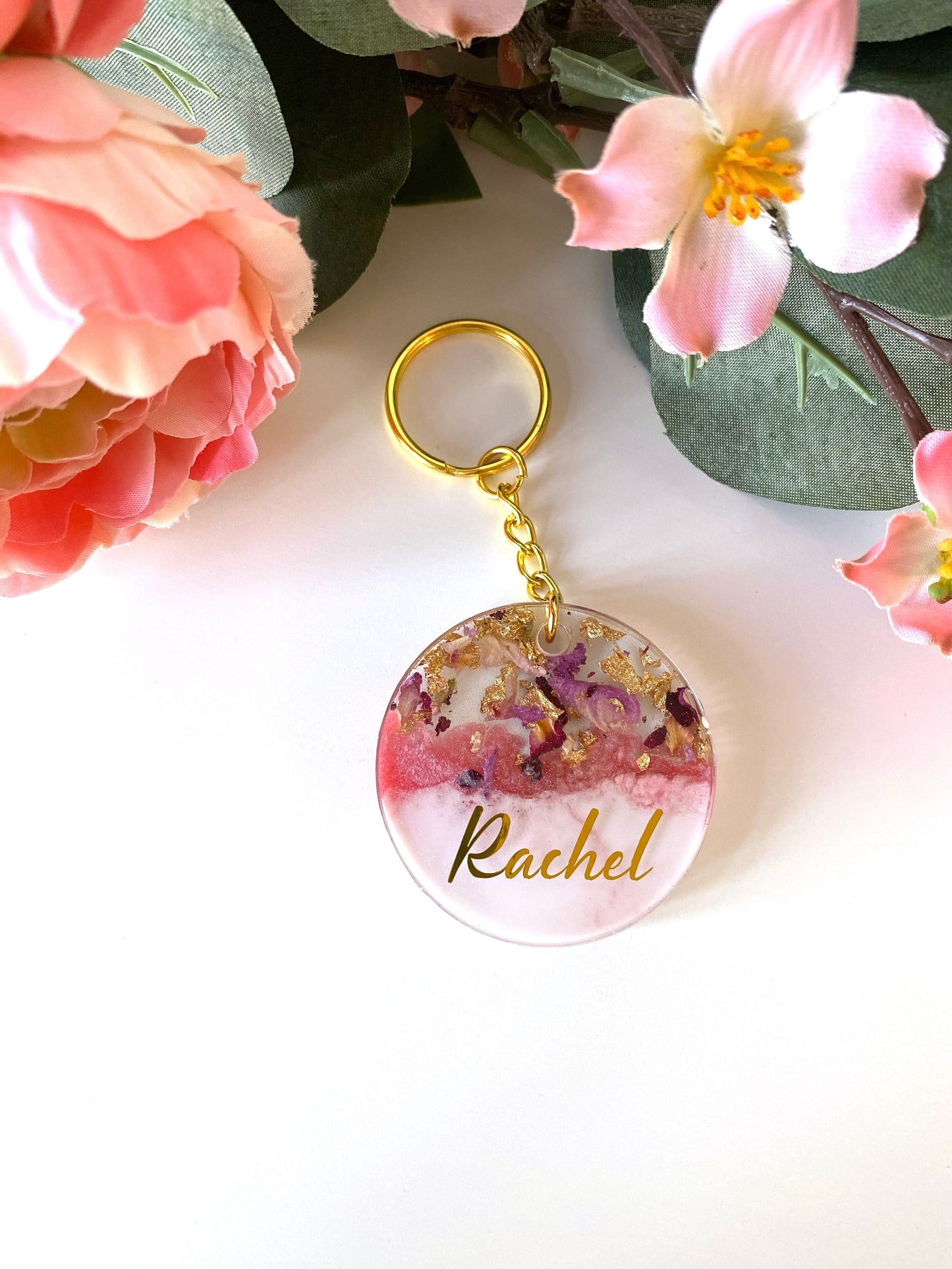 Pink and white round resin keychain with dried flowers and gold leaf, personalised in lowercase gold vinyl font, handmade resin keyring for gifts.