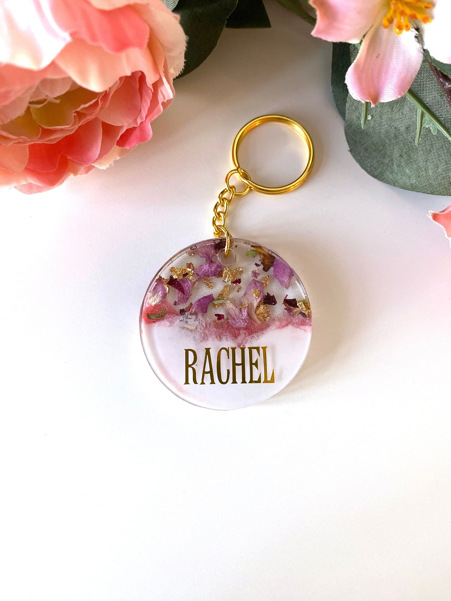 Pink and white round resin keychain with dried flowers and gold leaf, personalised in uppercase capital gold vinyl font, handmade resin keyring for gifts