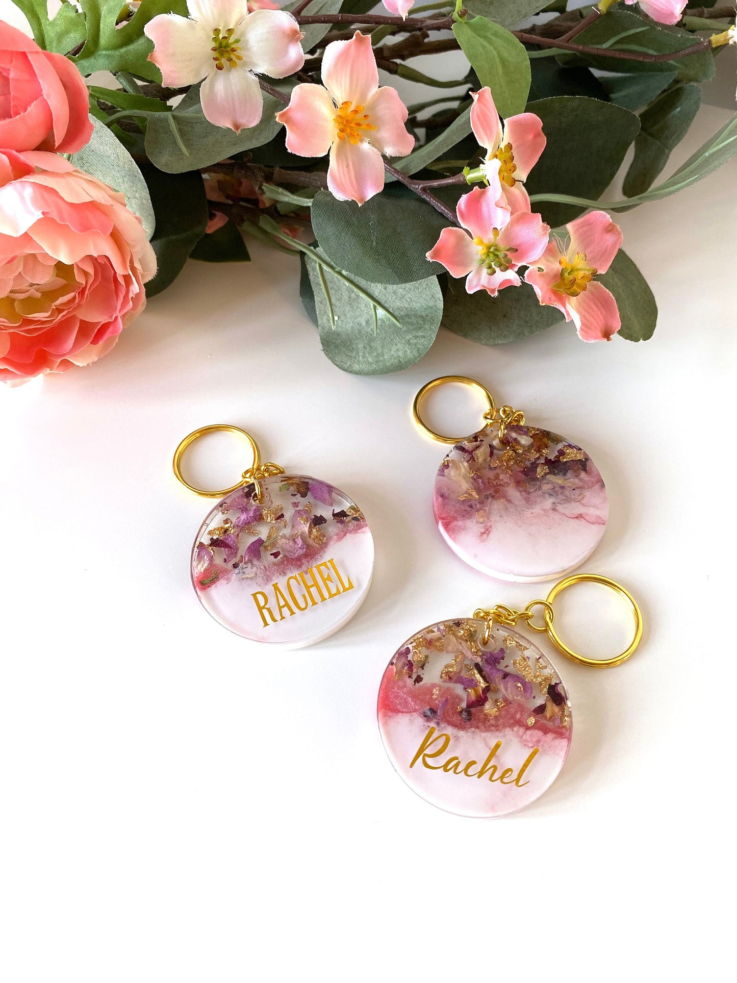 Pink and white round resin keychains with dried flowers and gold leaf, showing personalised and non-personalised options, handmade resin keyrings for gifts