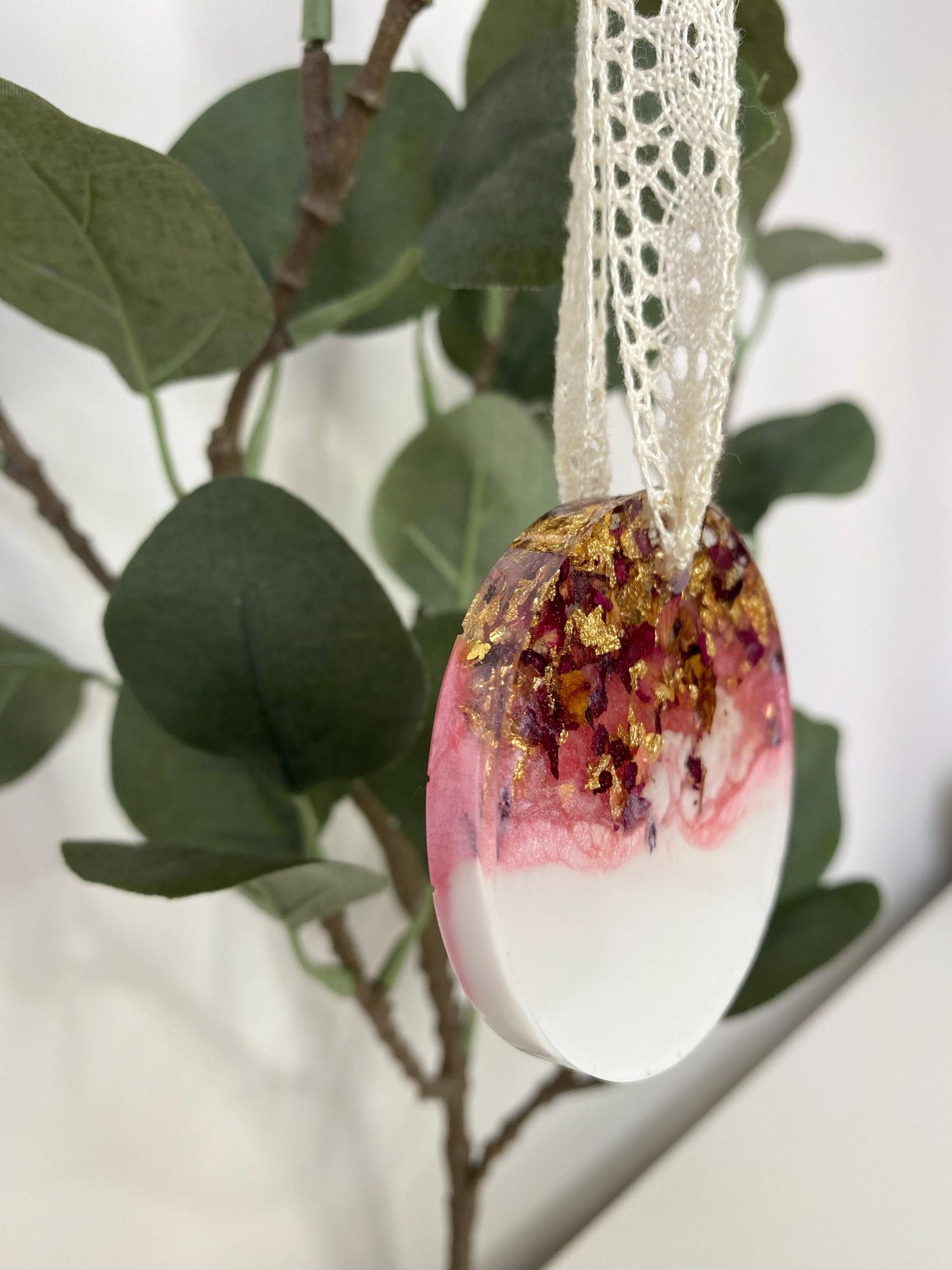 Non-personalised resin Christmas ornament with dried rose petals and gold leaf, angled to show thickness, pink and white colours, lace ribbon included.