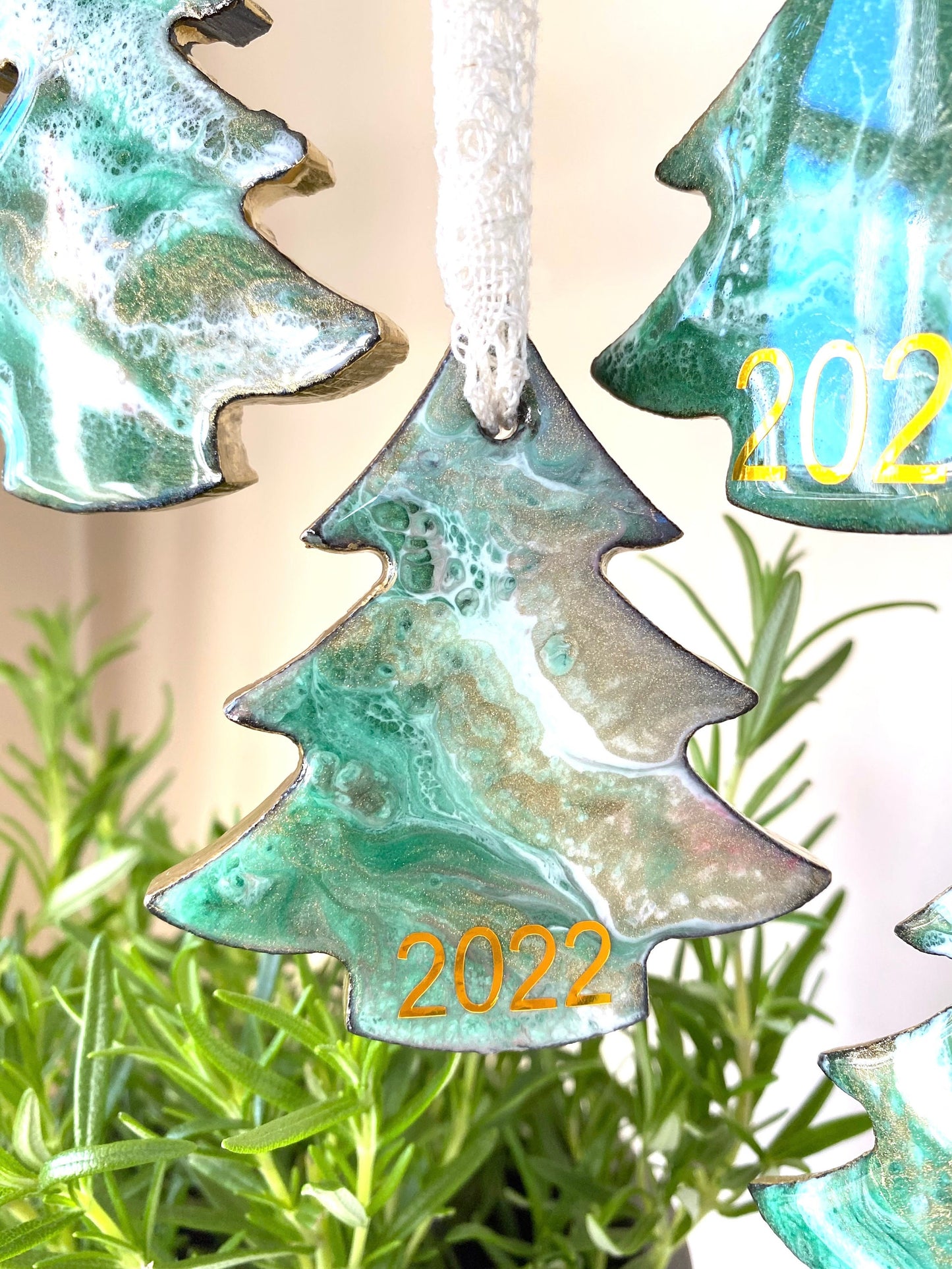 Decorative tree-shaped ornaments with '2025' on them, hanging against a green leafy background.