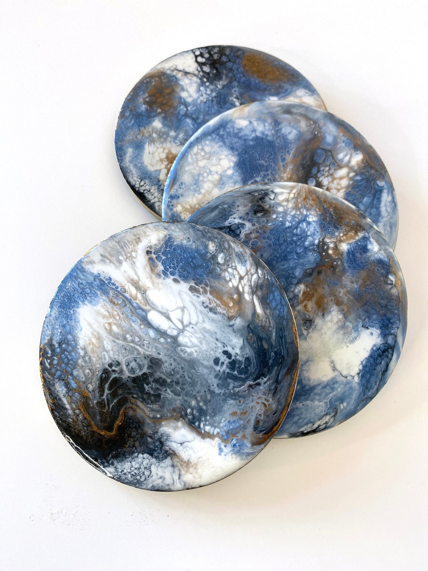 Top view of round slate resin coasters with unique blue, white, black, and gold epoxy designs and gold-painted edges, slightly overlapping to showcase handmade detail.