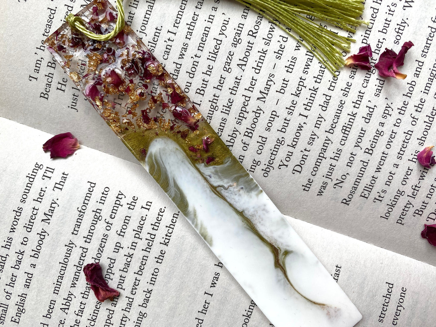 White and green resin bookmark with dried roses and gold leaf, non-personalised, placed inside an open book, featuring a green tassel, handmade bookmark for readers or gifts