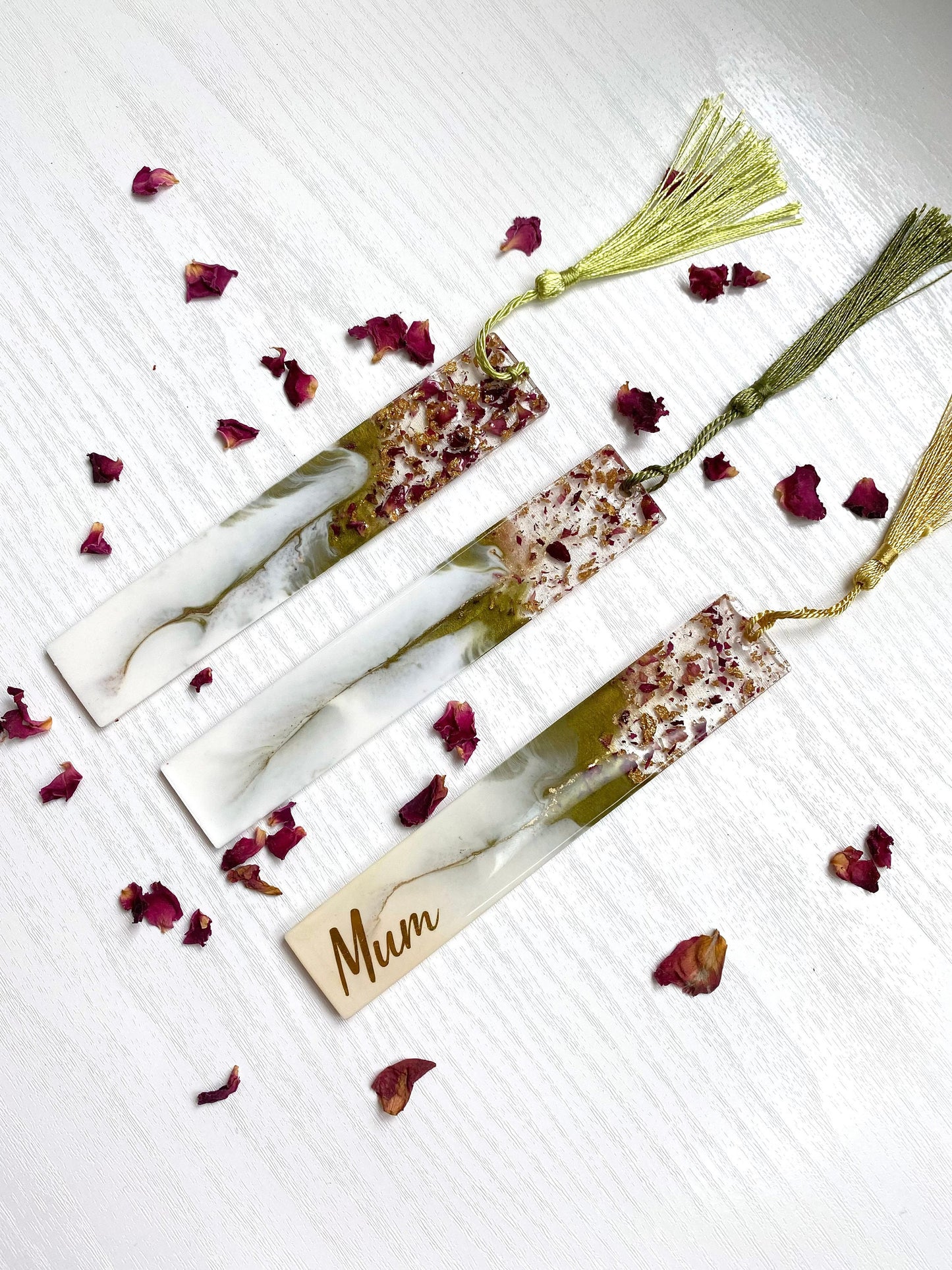 Three white and green resin bookmarks with dried roses and gold leaf, one personalised with gold vinyl and two non-personalised, each featuring a gold or green tassel, handmade bookmarks for readers or gifts.