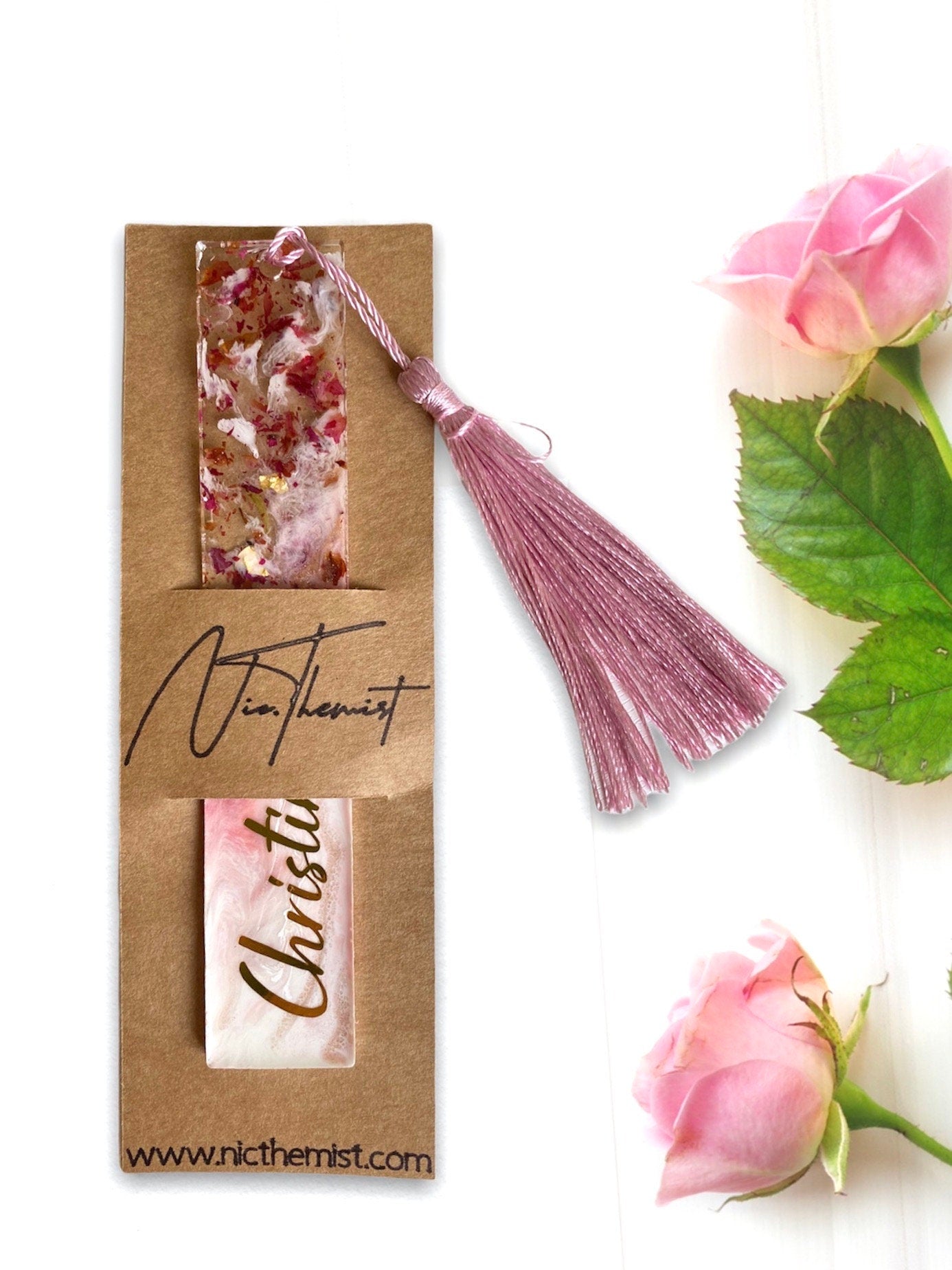 White and pink resin bookmark with dried roses and gold leaf, personalised with gold vinyl, inside a single packaging sleeve with logo, handmade bookmark for readers or gifts.