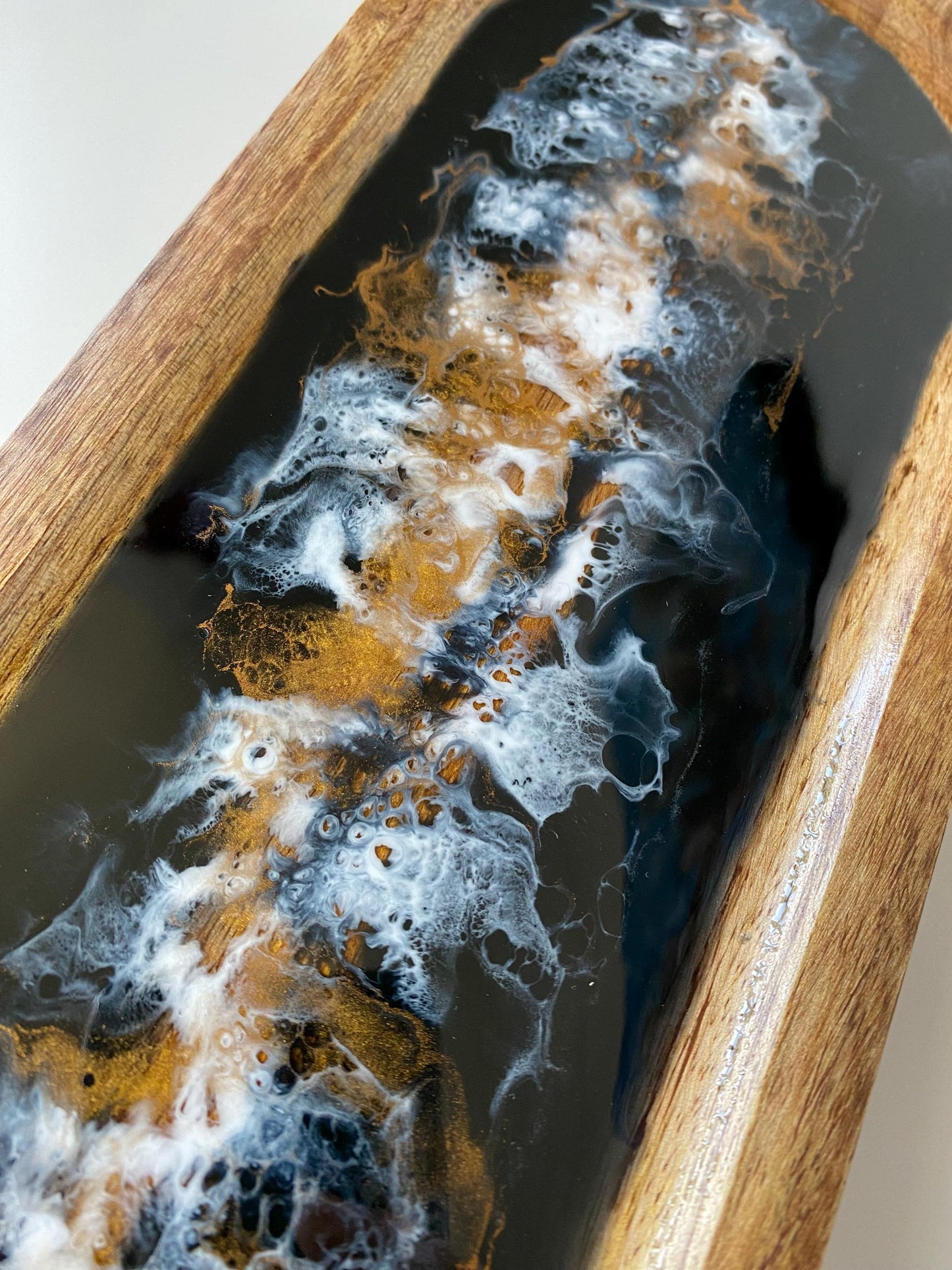 Super close-up of swirling epoxy resin on large handcrafted wooden oval tray, showcasing intricate black, white, and bronze patterns – unique artisan design for décor or serving.