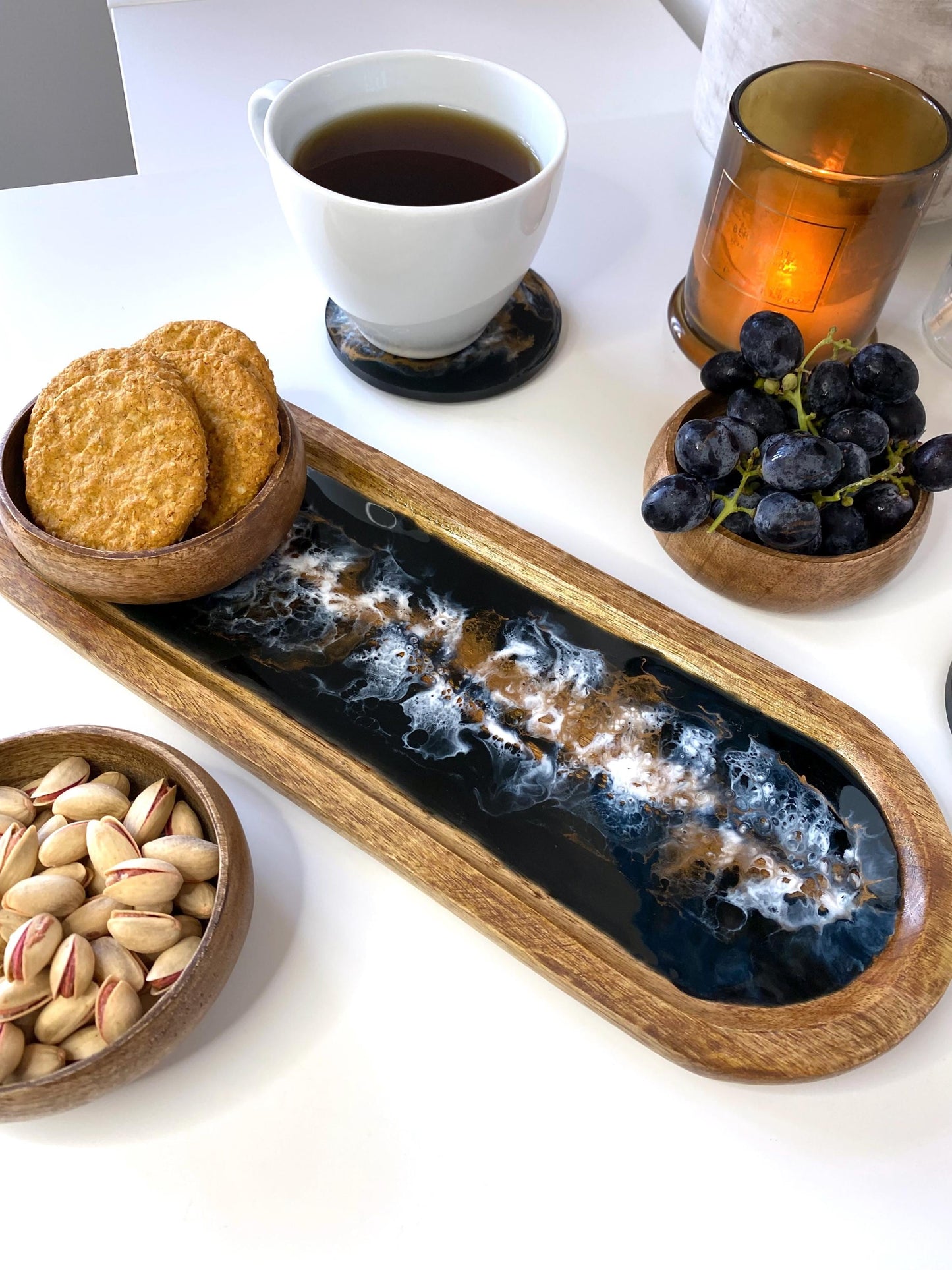 Handcrafted large wooden oval tray with epoxy resin details in black white and bronze, featuring one bowl with cookies, another with grapes, and a third with nuts, styled with a matching resin coaster holding a coffee cup and candle – perfect for serving or home décor.