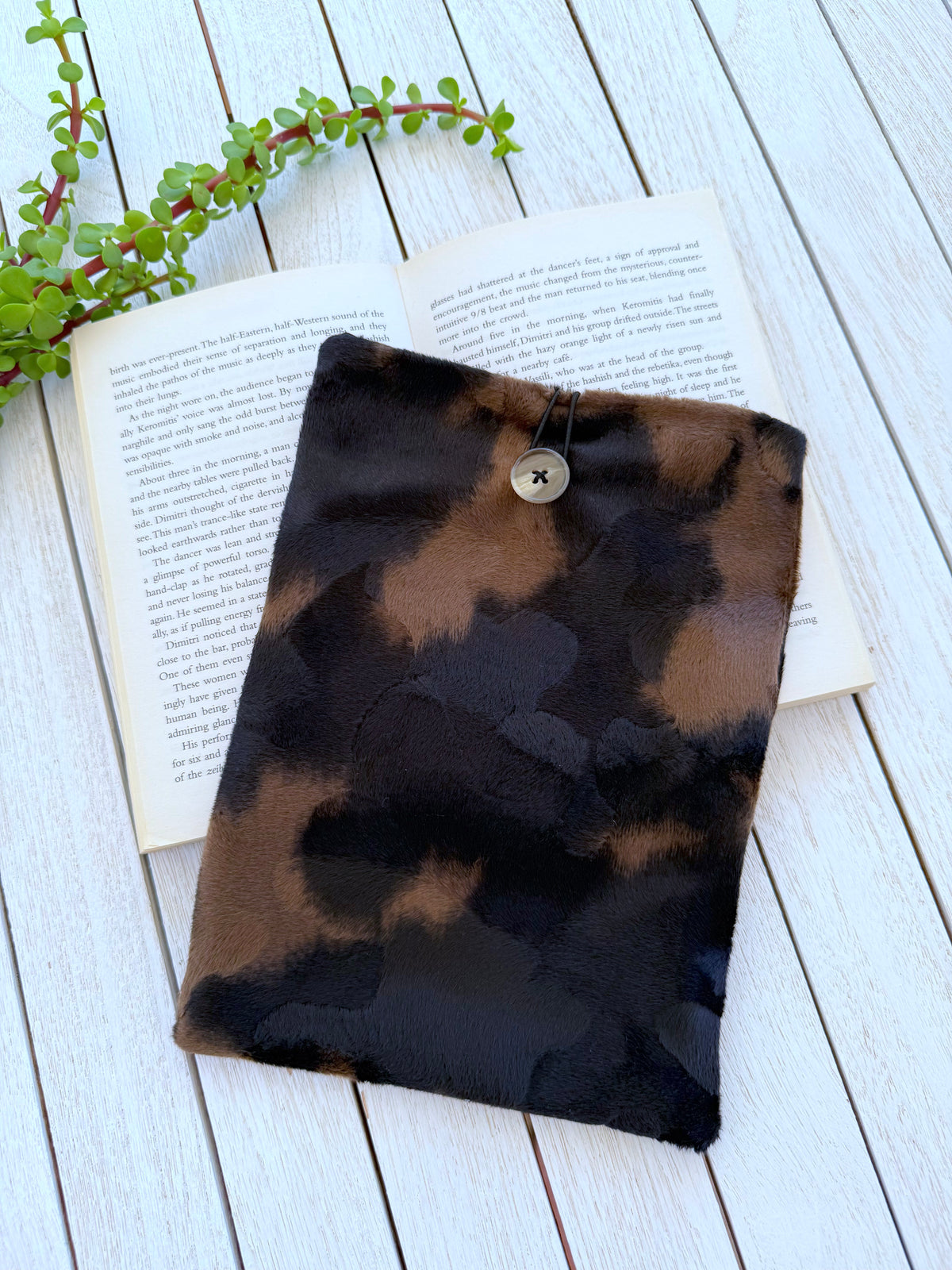 Black and brown velvet book sleeve with button closure displayed on an open paperback book, showing its size and animal print design.