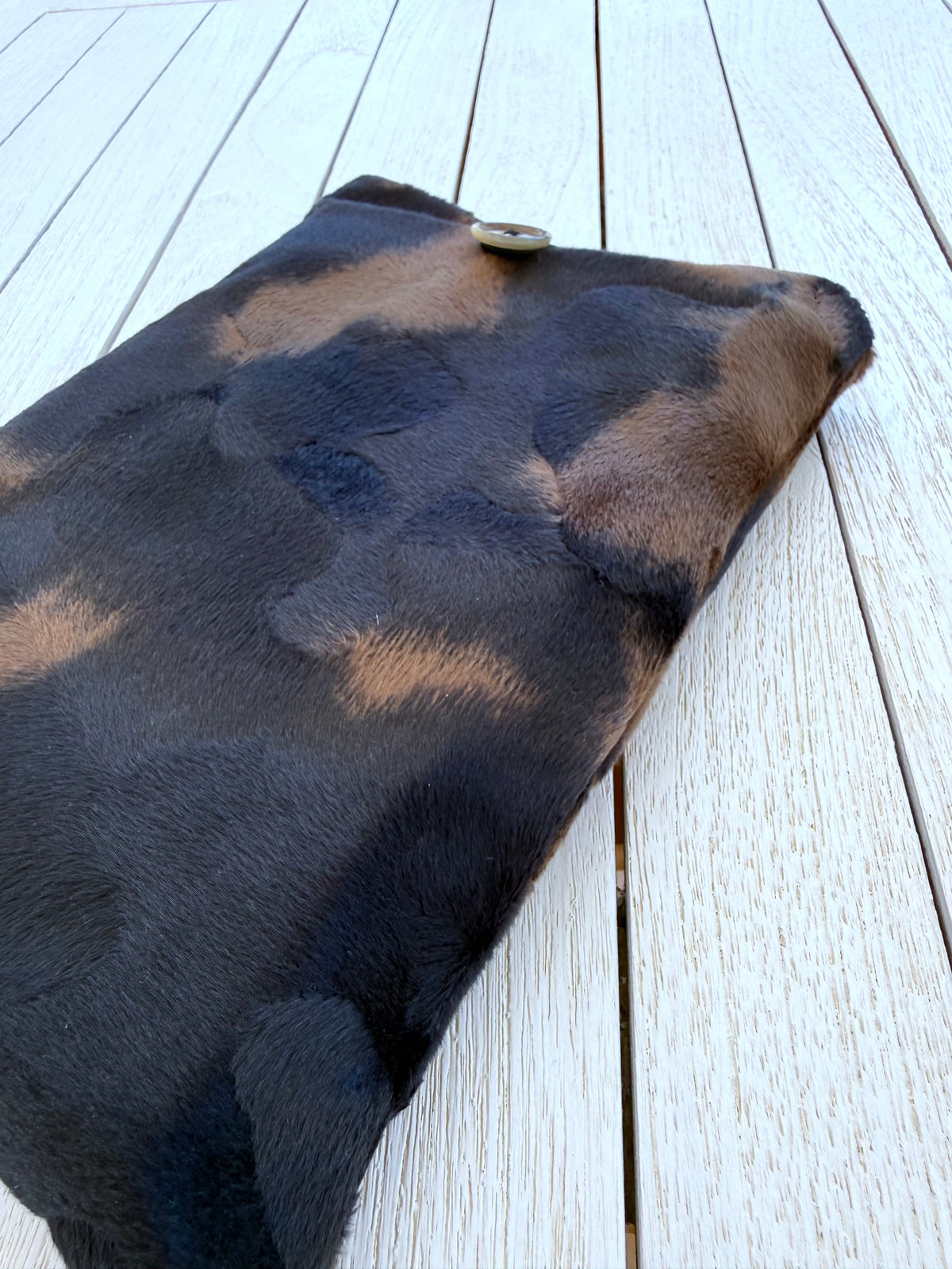 Angled view of a black and brown animal print velvet book sleeve showing its soft plush fabric and slim shape on a white wooden surface.