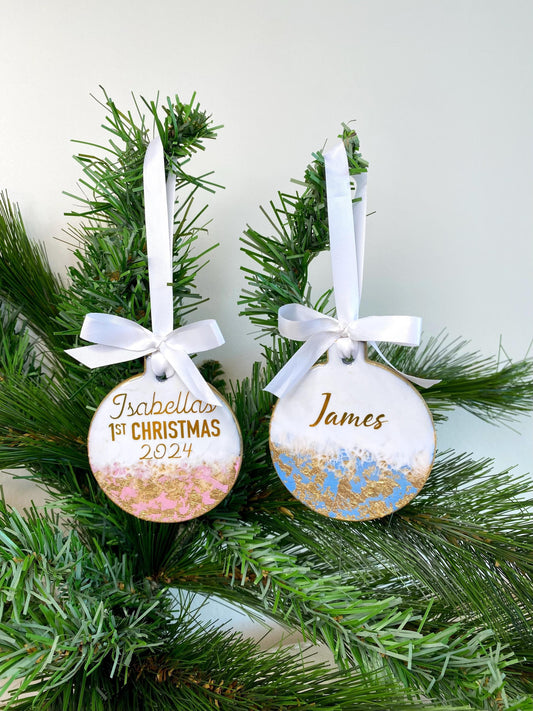 Blue and pink slate resin baby’s first Christmas ornaments hanging on a decorated Christmas tree, personalised with name and First Christmas text in gold