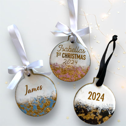 Three slate resin Baby’s First Christmas ornaments showing all personalisation options: blue with just a name, pink with baby's name and First Christmas, and black with the year 2025, all with hand-painted gold edges and white ribbons.