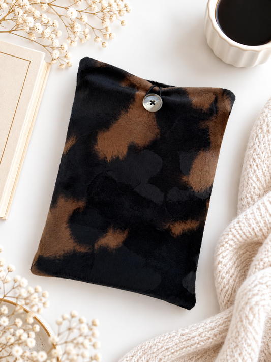 Handmade black and brown animal print velvet book sleeve with button closure, photographed beside a book, coffee and cream knitted blanket.
