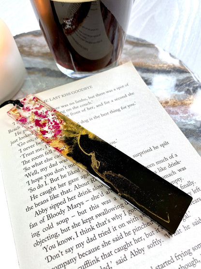 Decorative black and gold bookmark with dried rose flowers design on a book close up