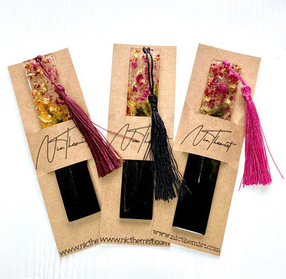 Black and gold resin bookmark with dried rose petals in branded packaging sleeve with Nic.Themist logo