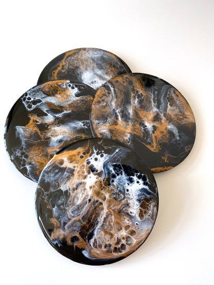 Close-up of four round resin and slate coasters in black, white and bronze, highlighting abstract modern design and handmade craftsmanship, decorative coasters for home or gifts