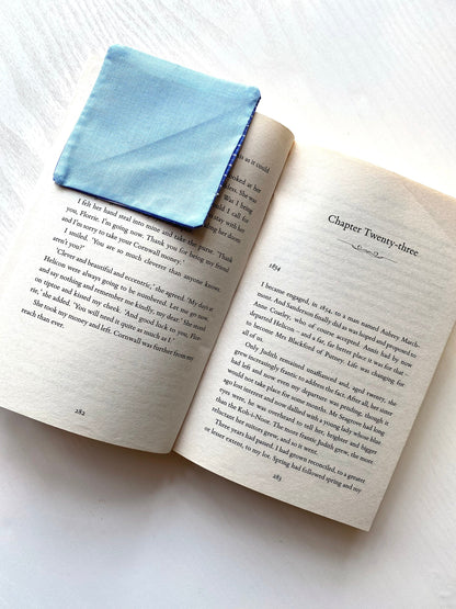 Open book with a blue fabric square on a white surface