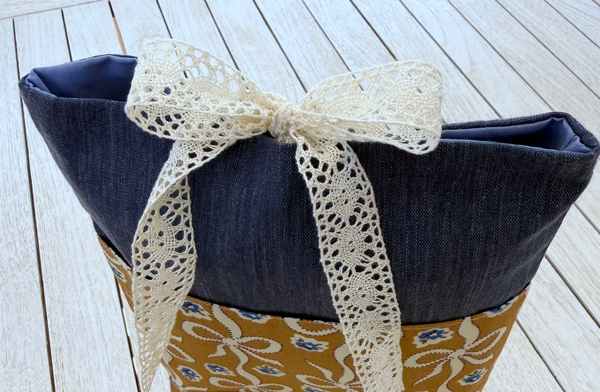 Close-up of the top of a navy denim-look book sleeve, showing the cream lace ribbon tied in a bow and the upper fabric opening.