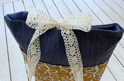 Close-up of the top of a navy denim-look book sleeve, showing the cream lace ribbon tied in a bow and the upper fabric opening.
