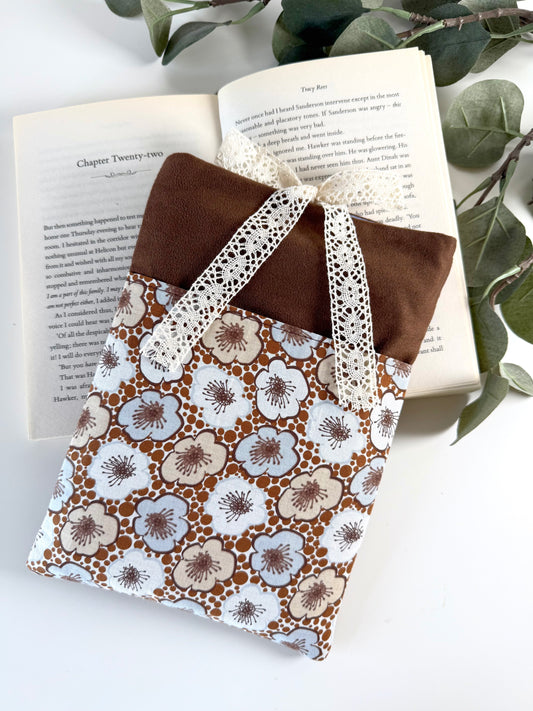 Handmade brown faux suede book sleeve with retro cream and pale blue floral front pocket and cream lace bow, displayed on an open paperback book.