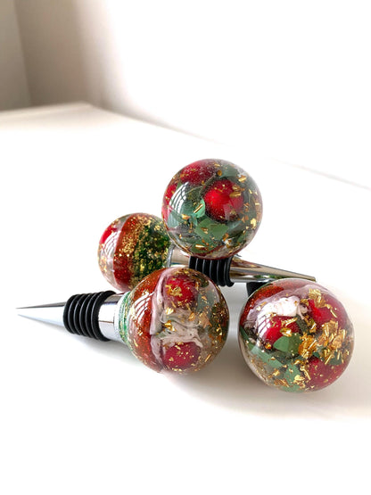 Four Christmas resin wine stoppers stacked showing detailed resin design with red berries, gold leaf, and glitter accents