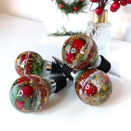 Four Christmas resin wine stoppers stacked showing red berries, gold leaf, and glitter details