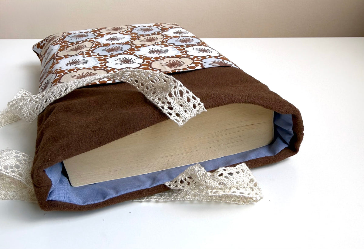 Close-up of the open top of a brown faux suede book sleeve showing a paperback book inside, blue fabric lining and floral cotton fabric.