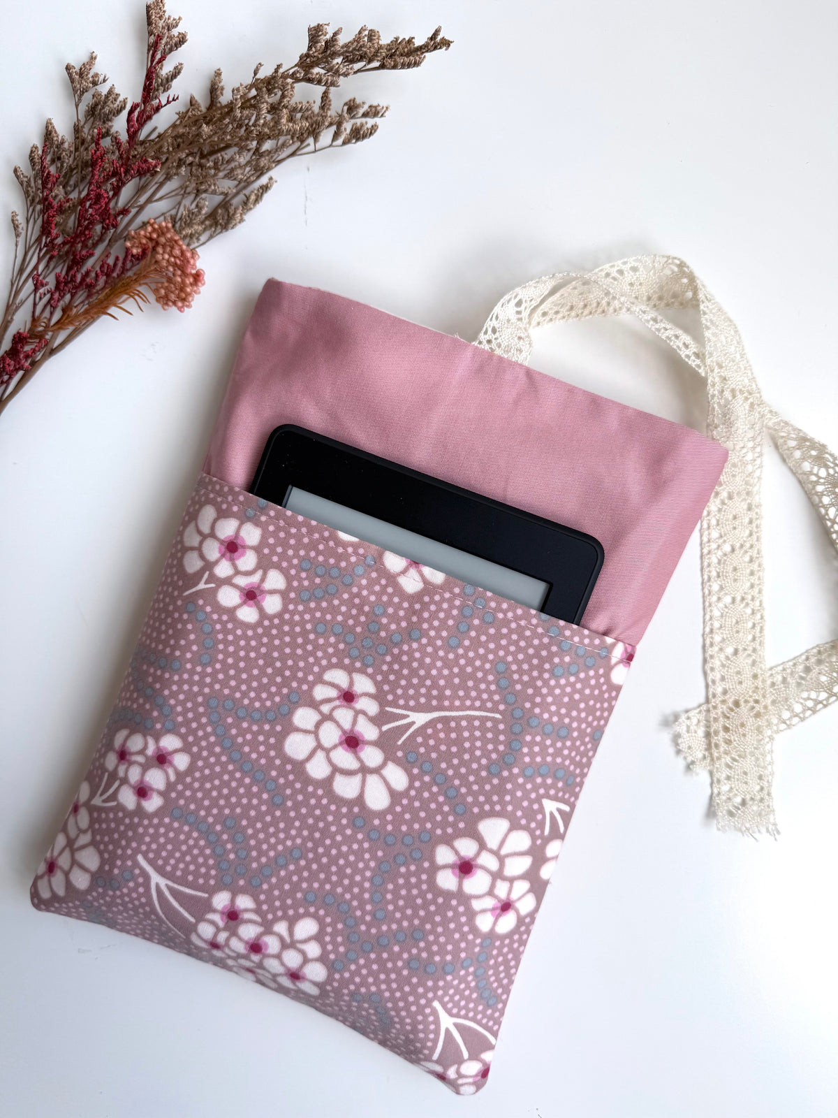 Close-up of a dusty pink fabric book sleeve with an e-reader tucked into the contrasting pink and purple floral front pocket.