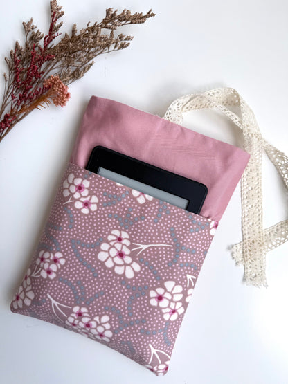 Close-up of a dusty pink fabric book sleeve with an e-reader tucked into the contrasting pink and purple floral front pocket.