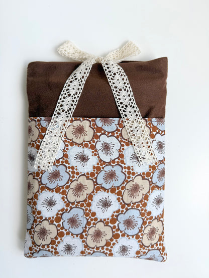 Front view of a handmade brown faux suede book sleeve with cream and pale blue retro floral cotton pocket and cream lace bow closure.