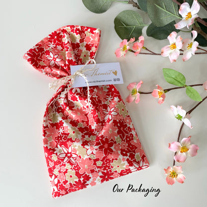 Fabric gift bag for handmade lace hair bow clips, used for packaging bows before shipping, displayed on white surface with flowers in the background
