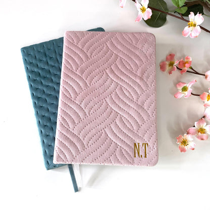 A5 luxury velvet notebooks with quilted covers, plain pink and teal versions, displayed on a white surface with flowers, both personalised with names or initials