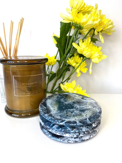 Set of four round resin art slate coasters, ocean-inspired design, stacked on top of each other on table, showing waves pattern, handmade decorative coasters for home or gifts.