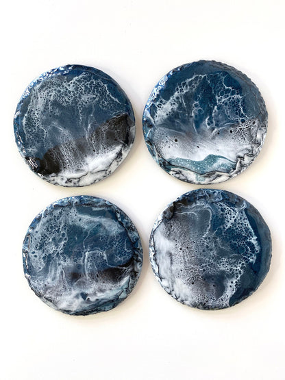 Top-down view of four round resin art slate coasters, ocean-inspired design, showing wave patterns on each coaster, handmade decorative coasters for home or gifts.