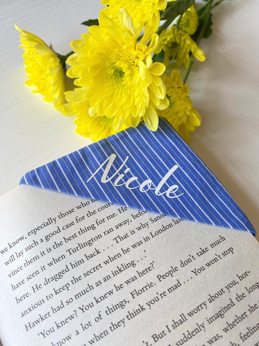 Personalised fabric corner bookmark in Blue Stripes design, placed on a book page with a name in white vinyl – handmade gift for book lovers or teachers.