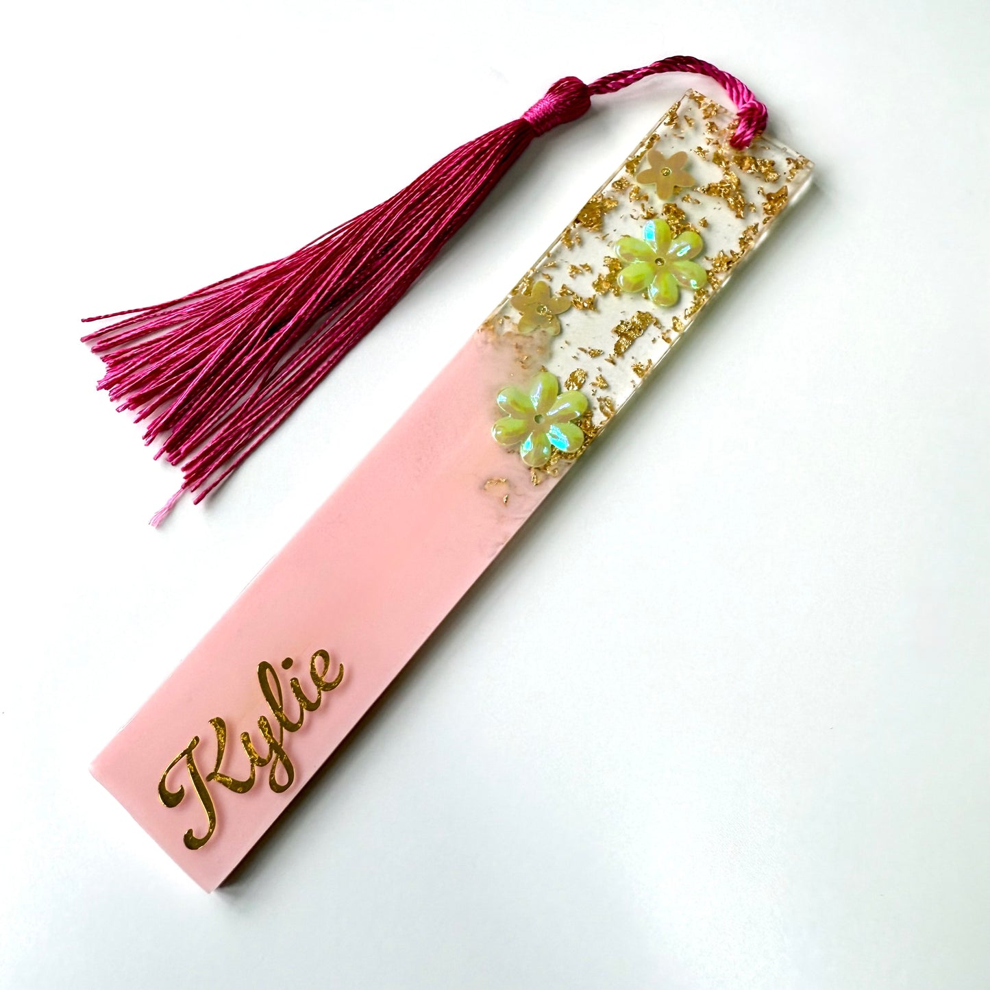 Personalised pink resin floral bookmark on a white surface, customised with gold vinyl and featuring a matching tassel.