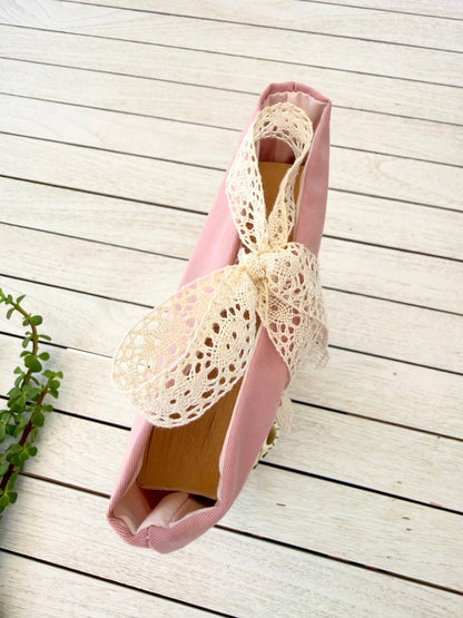Top view of a handmade dusty pink fabric book sleeve, showing the opening, floral fabric and cream lace ribbon bow closure.
